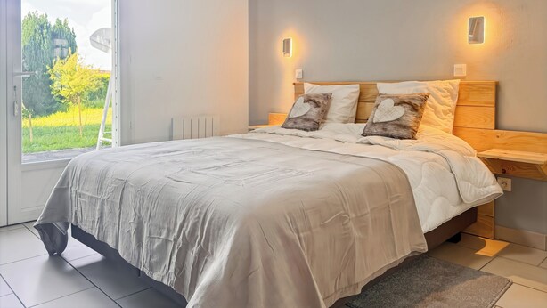 A bedroom with a large bed, two bedside tables, and a view of greenery through a window. - La Maison Bleue, on the Bay of the Somme, in a peaceful natural setting (Pendé)