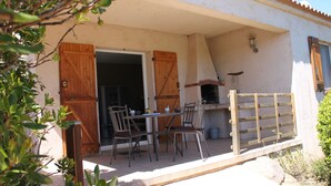 Une terrasse extérieure avec une table et des chaises, une porte en bois et une cheminée en briques.
