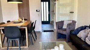 En moderne stue med et glas sofabord, et spiseområde med et træbord og stole, samt en sort lædersofa.