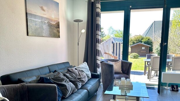 En moderne stue med en mørk lædersofa, et glasbord og udsigt til det fri via store skydedøre.