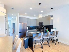 Una cocina moderna con electrodomésticos de acero inoxidable, una isla central con taburetes altos y luminarias colgantes.