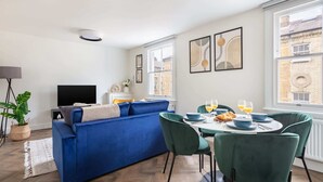 A modern living room with a blue sofa, dining table with chairs, and artwork on the walls. - Bright 1BR Near Museum of London (London)