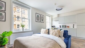 Un dormitorio moderno con una cama grande, una silla azul y vistas a un paisaje urbano a través de amplias ventanas.