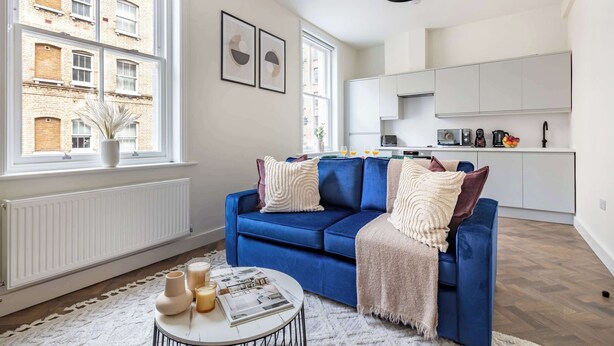 Una sala de estar moderna con un sofá azul, un radiador blanco y una cocina al fondo.