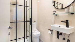 Un baño moderno con cabina de ducha de vidrio, inodoro blanco, lavamanos con grifo negro y espejo sobre el lavamanos.