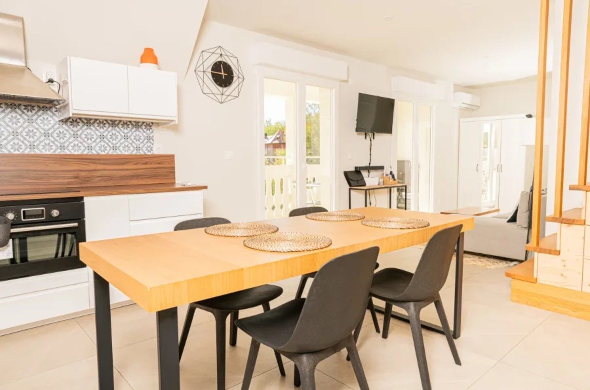 A modern kitchen with a wooden table and black chairs, a built-in oven, and a white cabinet.