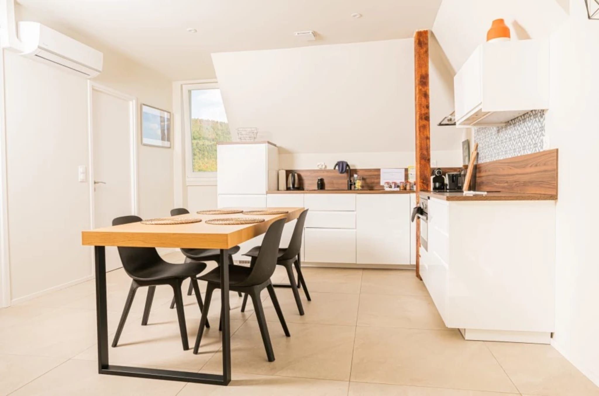 Une cuisine moderne avec des meubles blancs, un plan de travail en bois et un coin repas comprenant une table et des chaises.