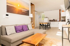 A modern living room with a sofa, a coffee table, and a painting of a sunset.