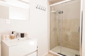 A modern bathroom with a glass-enclosed shower, a white vanity with toiletries, and a wall-mounted towel rack.