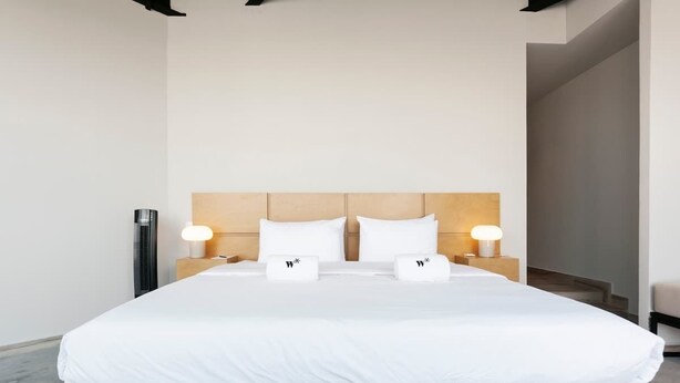 Moderni hotellihuone, jossa on suuri sänky, kaksi yöpöytää valaisimineen ja puinen sängynpääty.