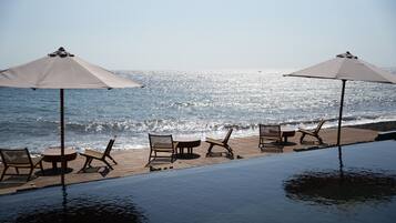 Una piscina infinita con sillones de descanso y sombrillas con vista al océano.