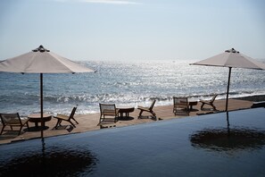 Una piscina infinita con sillones de descanso y sombrillas con vista al océano.