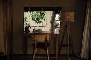 A wooden table with a chair, a floor lamp, and a window with a view of greenery. - Vela Tianyar Boutique Resort By Dhananjaya Hospitality (Kubu)