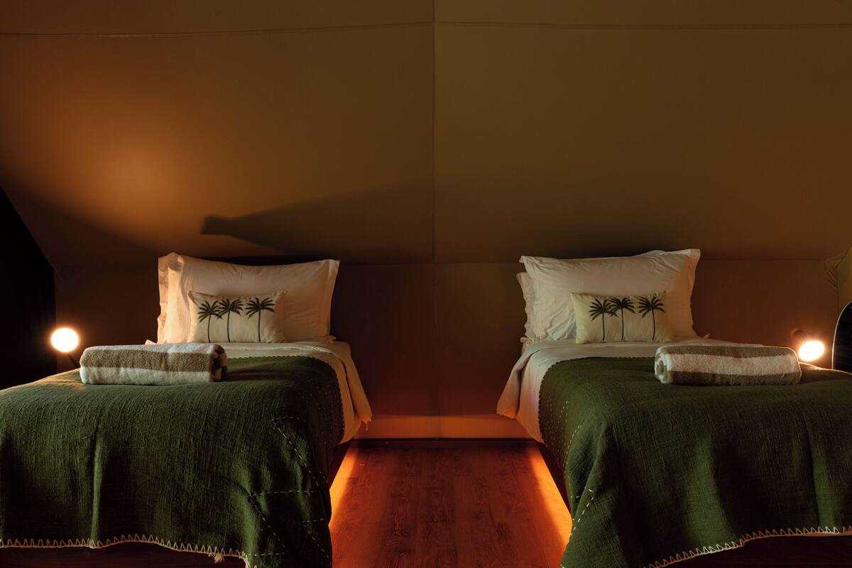 Ein Zimmer mit zwei Betten, jeweils mit grüner Decke und weißen Kissen, sowie Holzboden.