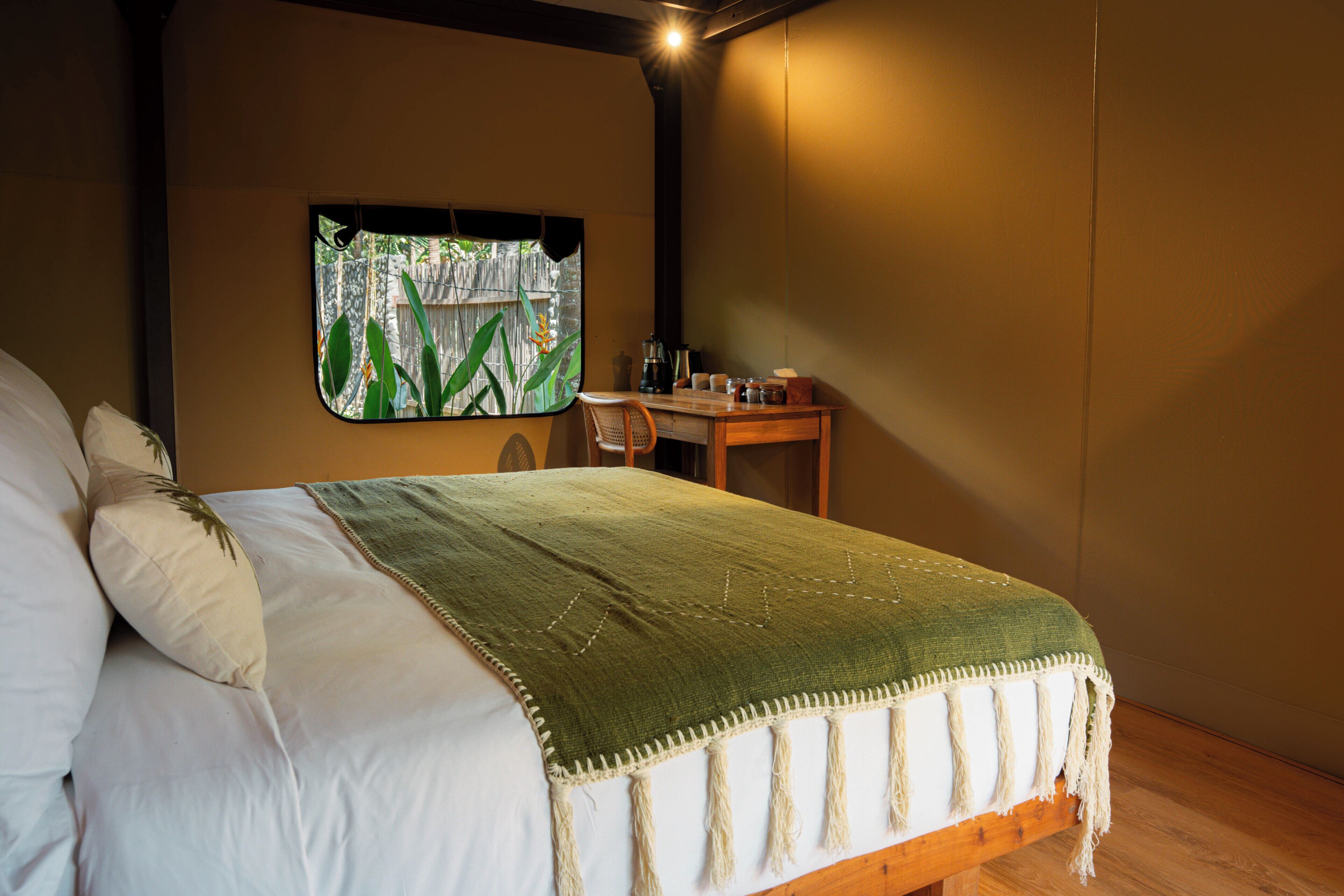 Un dormitorio con cama, ventana con vista a zonas verdes, escritorio de madera y una silla.