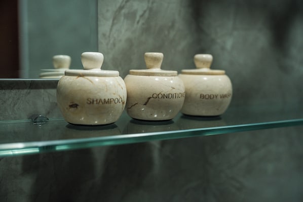 Three ceramic jars labeled 'SHAMPOO,' 'CONDITIONER,' and 'BODY WASH' on a glass shelf. - Vela Tianyar Boutique Resort By Dhananjaya Hospitality (Kubu)