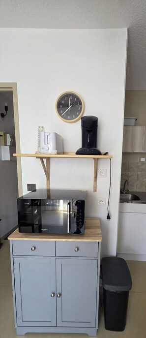A kitchenette with a microwave, coffee maker, and a clock on the wall.