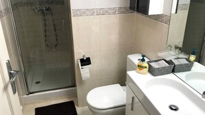 Un baño con cabina de ducha de vidrio, inodoro, lavabo con espejo y dispensador de jabón.