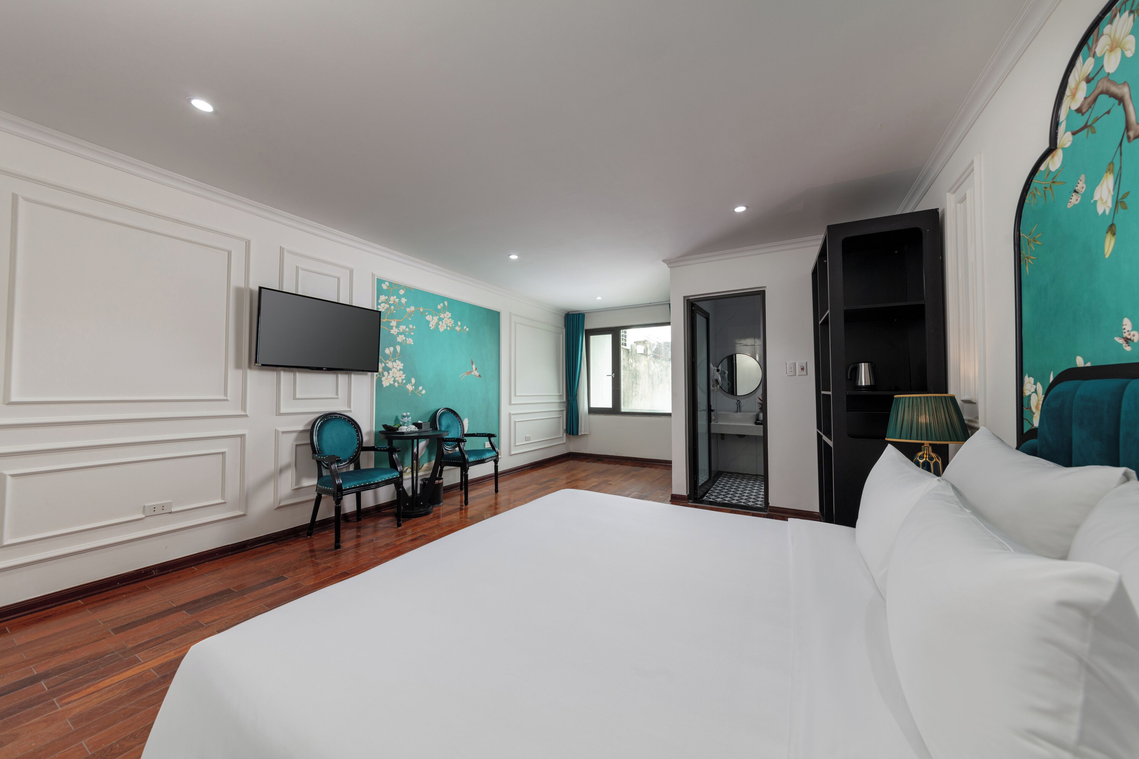 A hotel room with a large bed, a desk with chairs, a TV mounted on the wall, and a door leading to a bathroom.