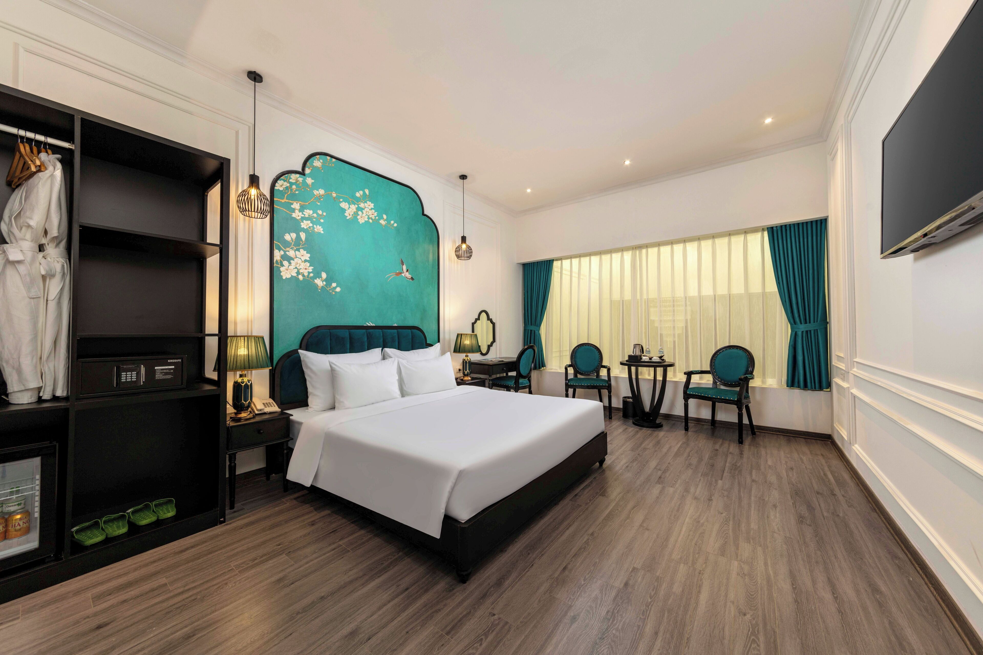 A hotel room with a large bed, a desk, two chairs, a TV, and a wardrobe.