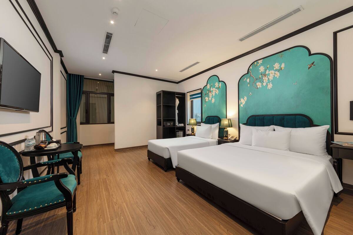 A hotel room with a large bed, two bedside tables with lamps, a TV, a desk with a chair, and a wardrobe.