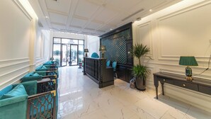 A spacious lobby with a high ceiling, a reception desk, teal seating, and a marble floor.