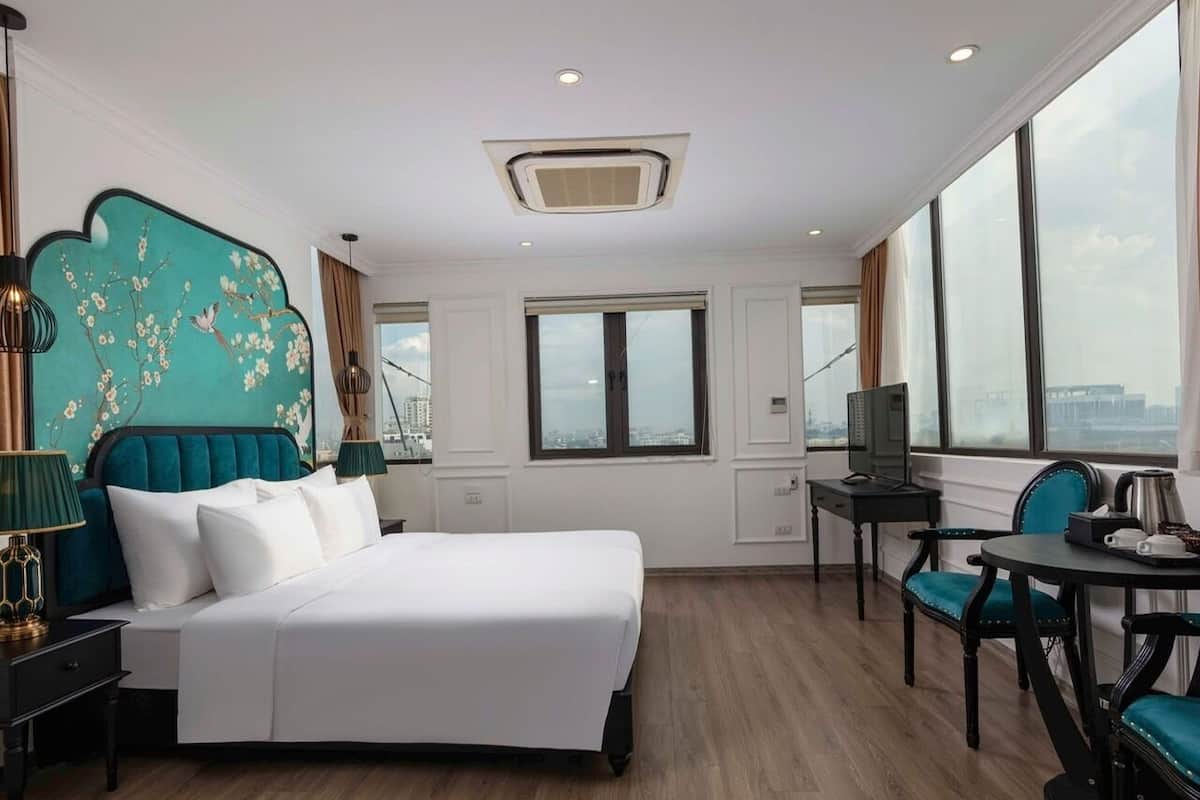 A hotel room with a bed, a desk, a chair, and a view of the city.