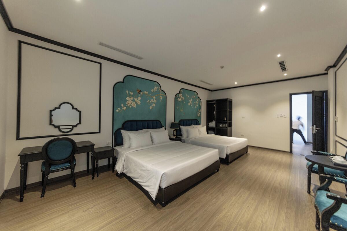 Habitación de hotel con dos camas, un escritorio, una silla y una mesita.