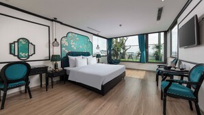 A modern hotel room with a large bed, two chairs, a desk, and a TV.