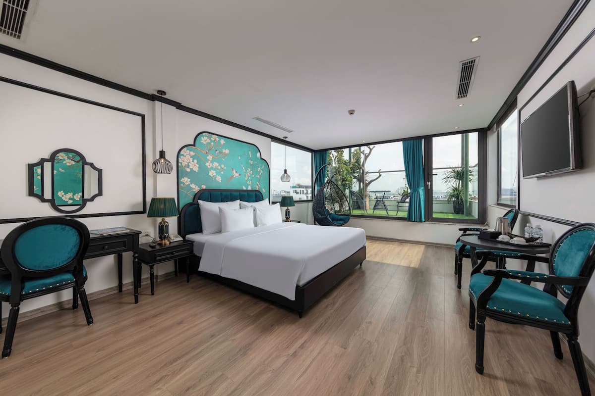 A modern hotel room with a large bed, two chairs, a desk, and a TV.