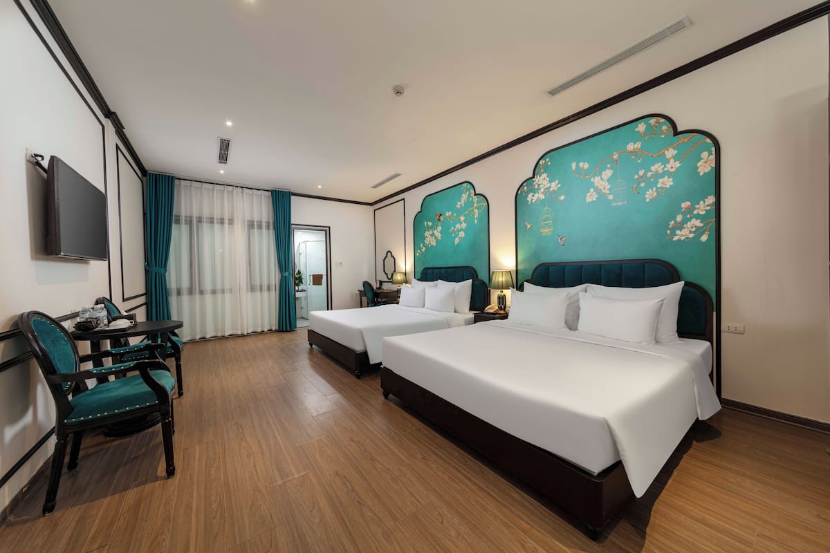 A hotel room with two beds, a desk with a chair, a TV, and a window with curtains.