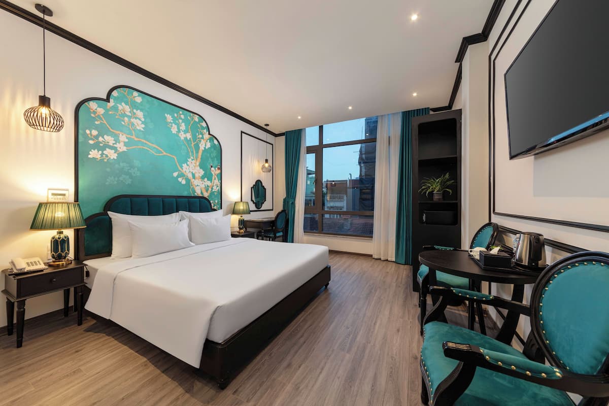 A hotel room with a large bed, a desk with a chair, a TV, and a window with curtains.