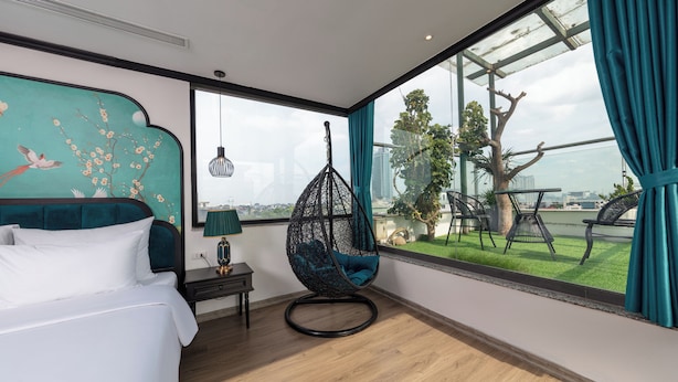 A modern hotel room with a large window, a hanging chair, a bed, and a decorative wall mural.