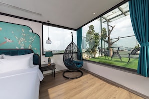 Een moderne hotelkamer met een groot raam, een hangstoel, een bed en een decoratief muurschildering.