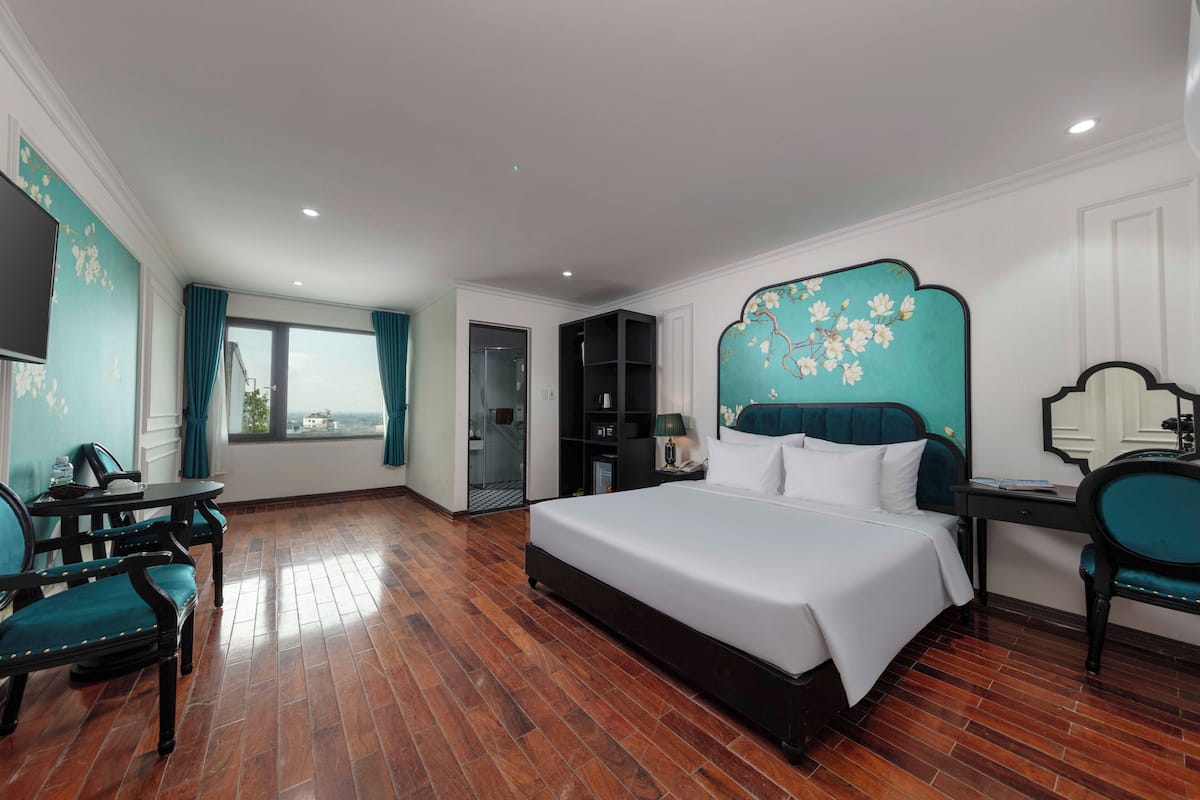 A hotel room with a large bed, a desk, a chair, and a view of the city through the window.