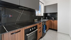 Une cuisine moderne avec un plan de travail noir, des armoires en bois, un four encastré et un lave-linge.