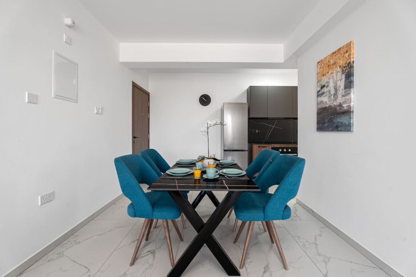 A modern dining area with a black table, blue chairs, and a clock on the wall.