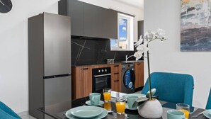 Une cuisine compacte dotée d’appareils électroménagers modernes, un coin repas avec une table mise pour le petit-déjeuner et une fenêtre offrant une vue agréable.