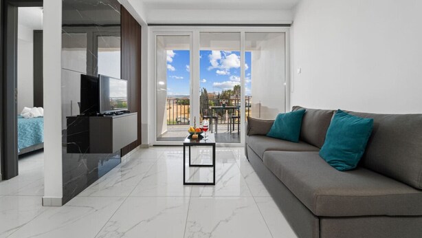 Un salon moderne avec un canapé, une table basse et un téléviseur. Il y a un balcon avec vue sur la ville.