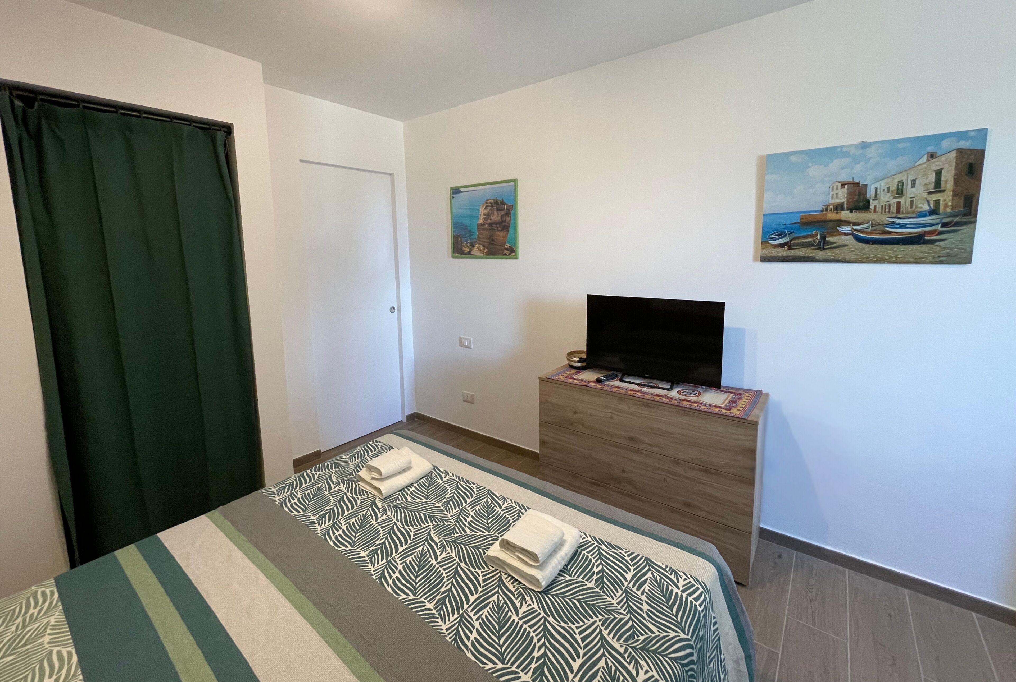 A hotel room with a bed, a TV on a wooden dresser, and two paintings on the wall.