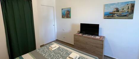 A hotel room with a bed, a TV on a wooden dresser, and two paintings on the wall.