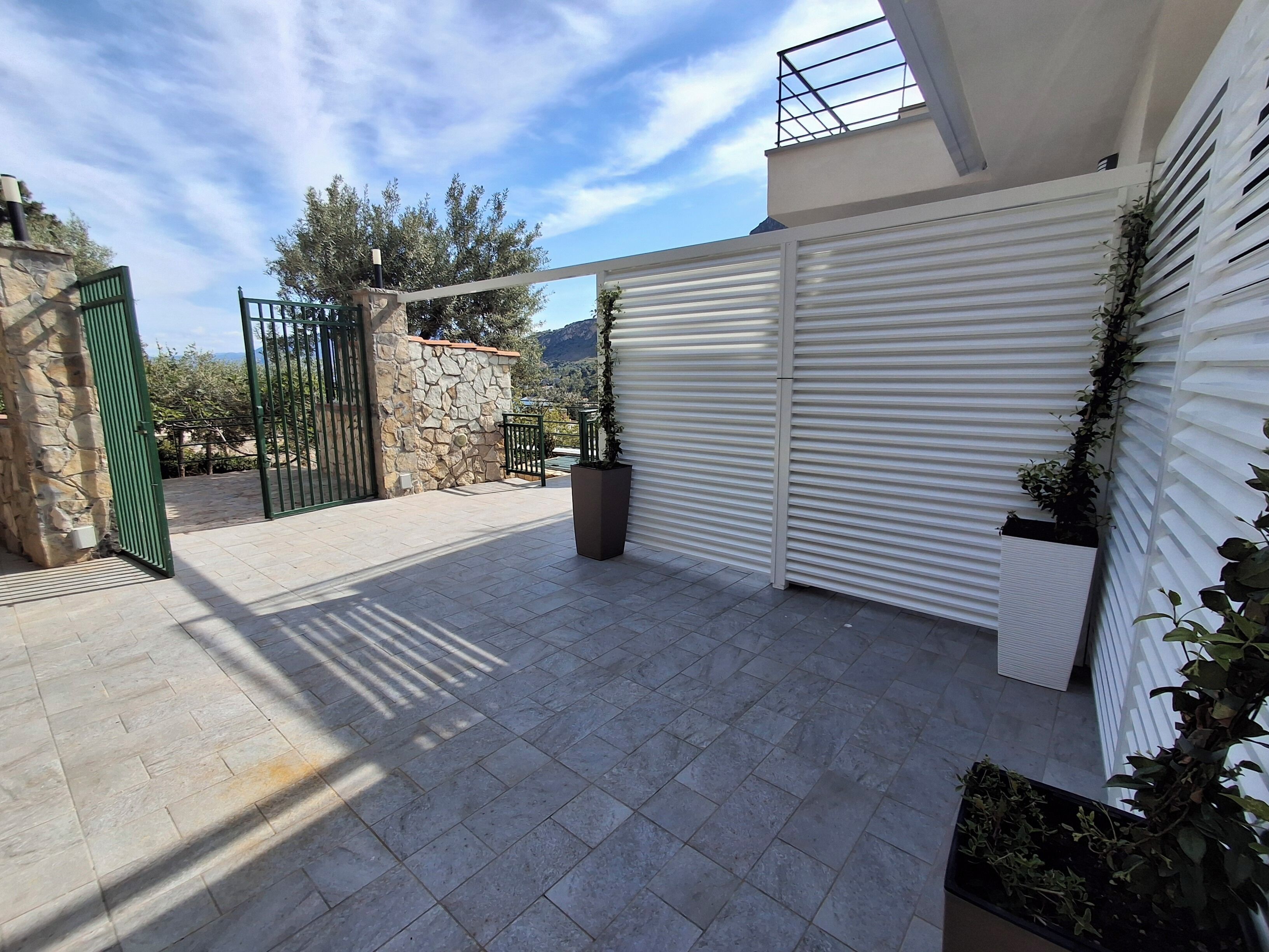 A covered outdoor patio with a stone wall, a green gate, and potted plants.