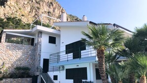 Una casa de dos pisos con fachada de piedra, piscina y palmeras.