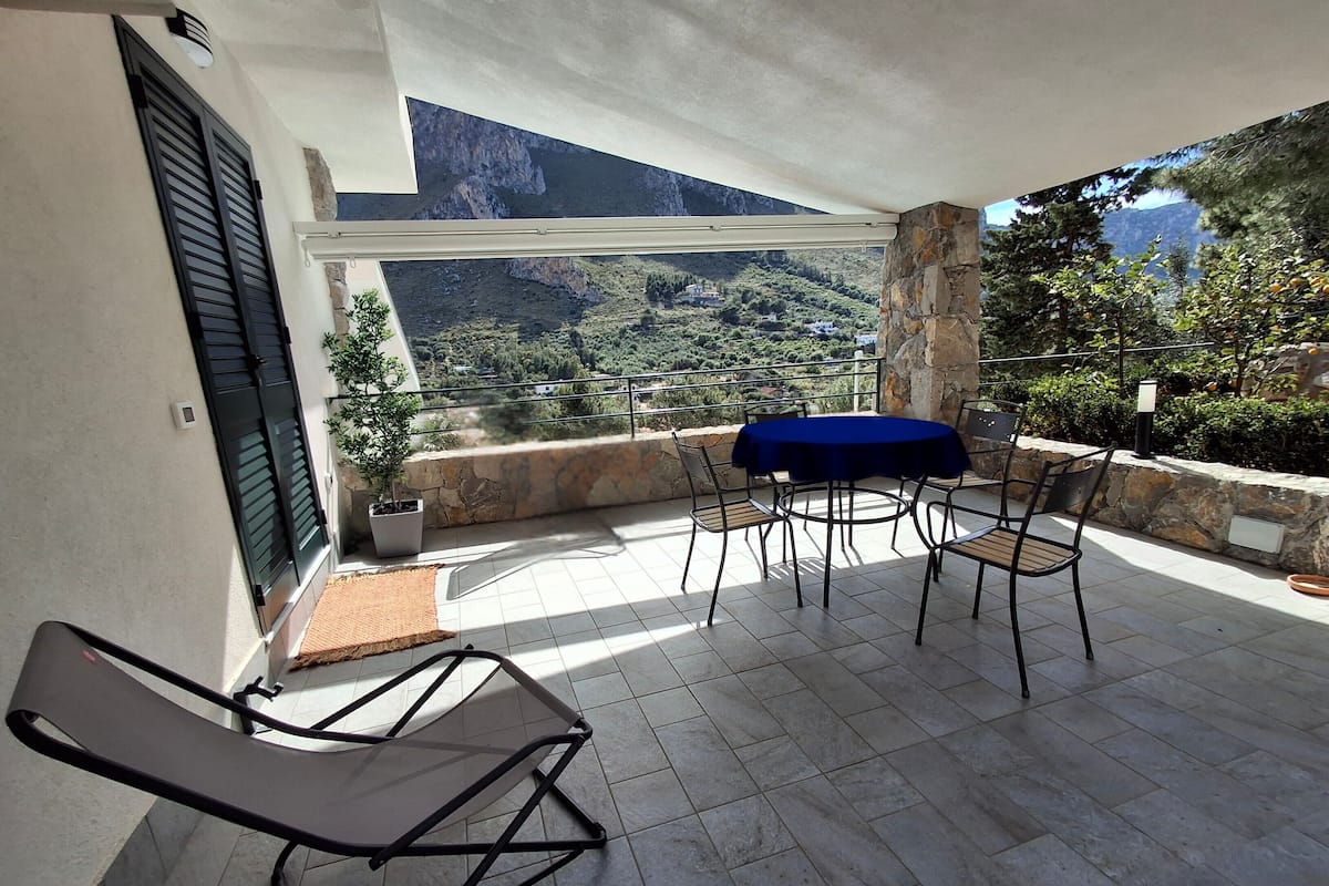 Un balcone con tavolo e sedie, una pianta in vaso e vista su un paesaggio montuoso.