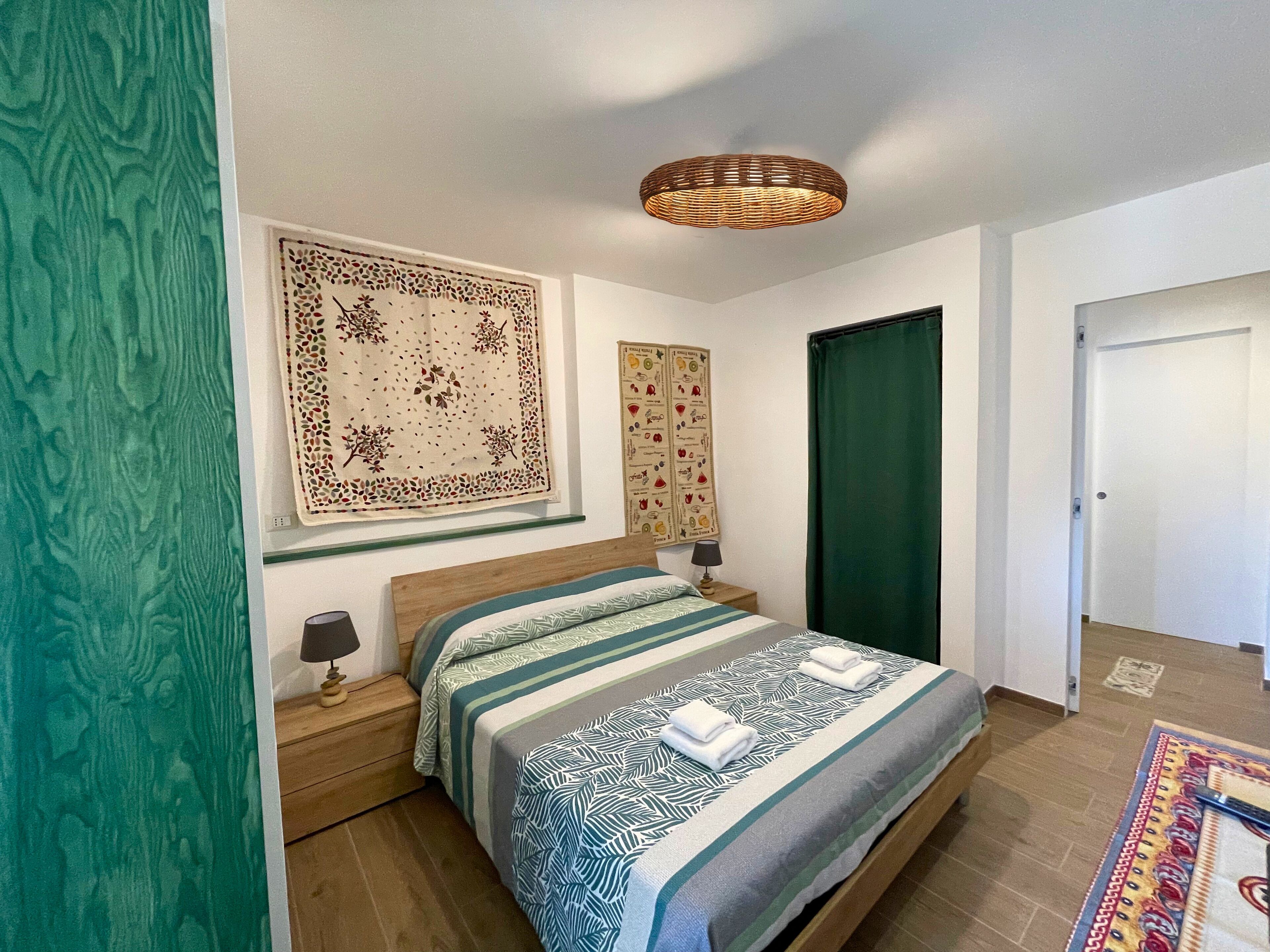 A neatly arranged bedroom with a bed, bedside tables, a hanging light fixture, and a door.