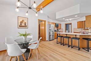 A modern kitchen with a central island, bar stools, and a dining area with a glass table and chairs.