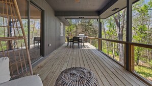 Eine Holzterrasse mit Deckenventilator, einem Tisch mit Stühlen und Blick auf Bäume.