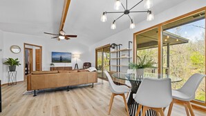 Ein modernes Wohnzimmer mit einer Couch, einem Esstisch, Stühlen und einem großen Fenster.