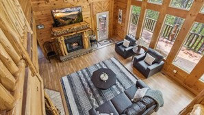 L’intérieur d’un chalet en bois comprend une cheminée, un téléviseur et un coin salon avec un tapis et des coussins.