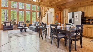 Un vaste espace de vie doté d’une cheminée, d’une table à manger avec des chaises, et d’un coin cuisine avec des meubles en bois et un réfrigérateur.